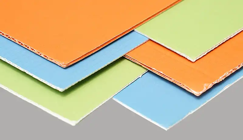 Stacked sheets of F flute corrugated paper in orange, blue, and green