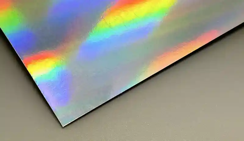 Holographic paper sheet reflecting rainbow colors on a smooth surface