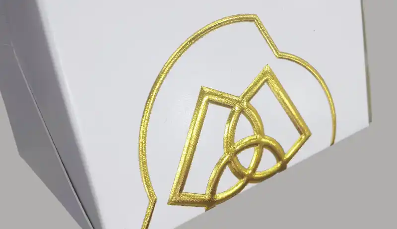 Gold 3D foil stamping on white rigid box with embossed effect.