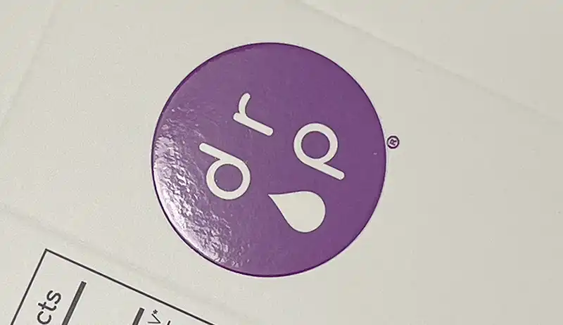 Glossy spot UV coating on purple logo over matte white surface.