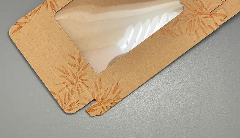 Kraft paperboard box with clear PET window and printed leaf design.