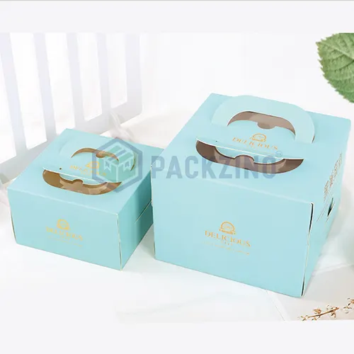 Two pastel blue cube-shaped cake boxes with handle and gold foil logo