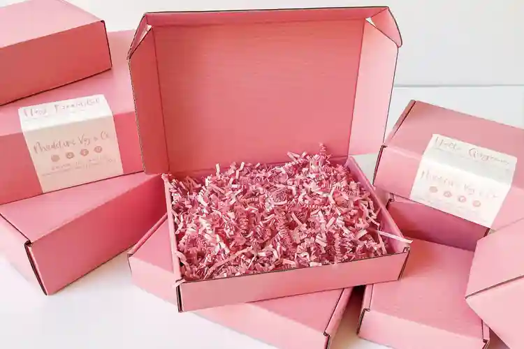Shipping packaging for skincare with pink corrugated boxes and protective paper filler inside.