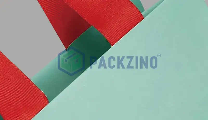 Red polyester handle taped onto green paper bag top edge