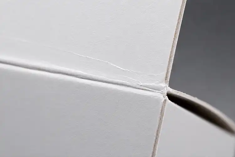 FBB folding carton crease showing fine white stress lines and moderate surface cracking under folding pressure